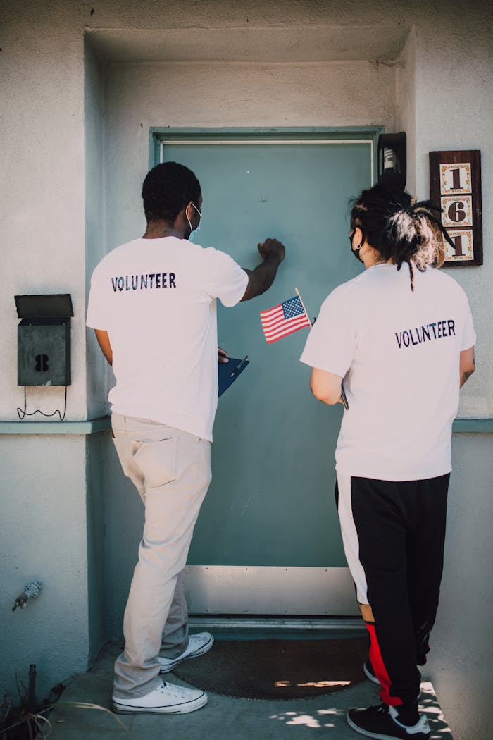 heros-img Two volunteers knocking on a residential door holding an American flag, promoting community engagement.