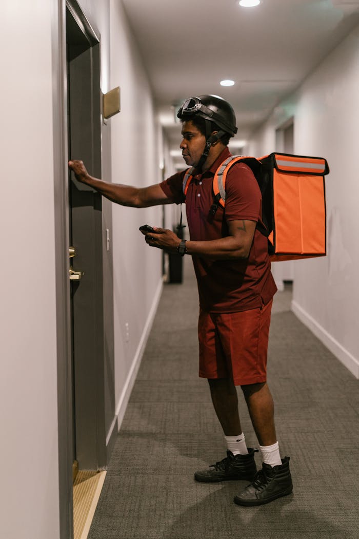 about-us-01 Courier with helmet and delivery bag knocking on an apartment door.